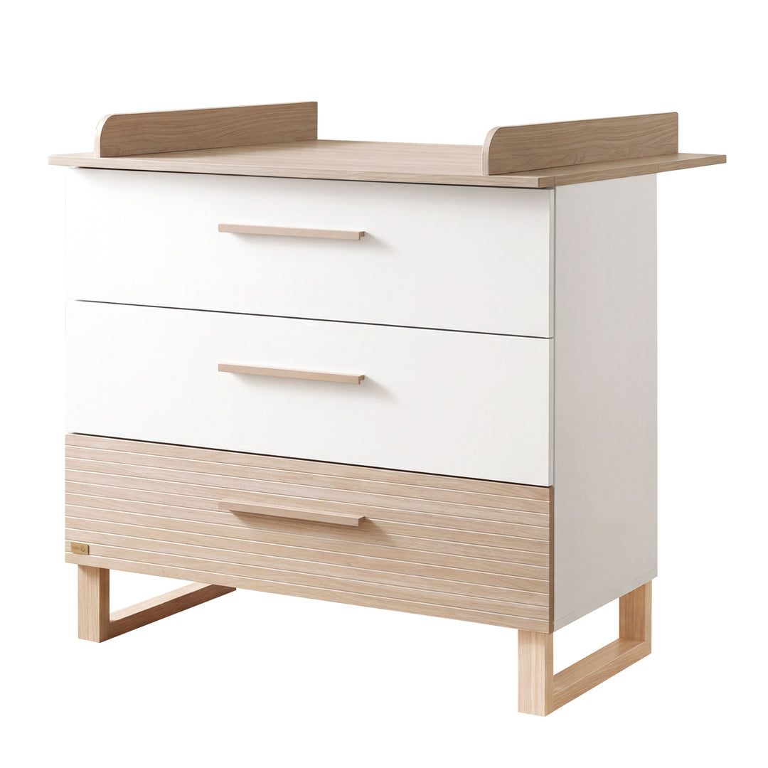 Wickelkommode "Noah" in Weiß/Eichenoptik mit 2 weißen Schubladen und 1 Holzdekor-Schublade, Aufsatzbrett mit seitlichen Wickelrändern und Kufengestell – Freisteller, Ansicht von schräg vorne (1/13)
