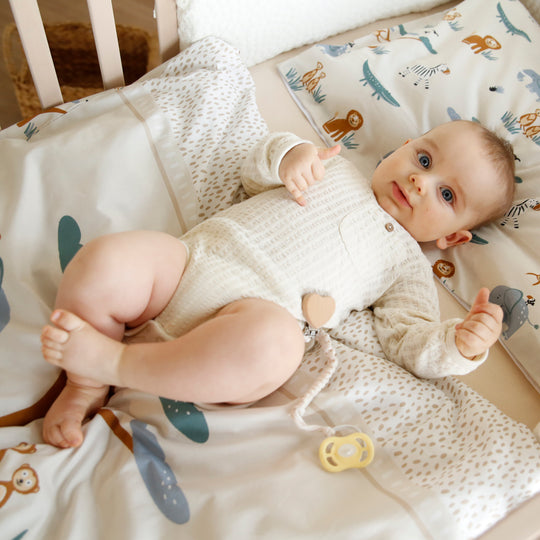 Baby liegt im Bettchen auf der Wiegenbettwäsche "Savanna Friends" mit Tiermuster in Beige und Blau