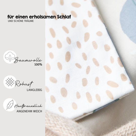 Nahaufnahme des gepunkteten Stoffs der Wiegenbettwäsche "Savanna Friends" mit Hinweis "für einen erholsamen Schlaf und schöne Träume" sowie Produktvorteilen: 100% Baumwolle, robust und langlebig, hautfreundlich und angenehm weich