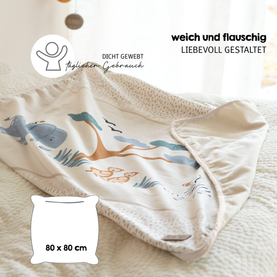 Babydecke "Savanna Friends" auf einem Bett drapiert mit Hinweisen "weich und flauschig" und "liebevoll gestaltet", Maßangabe 80 x 80 cm