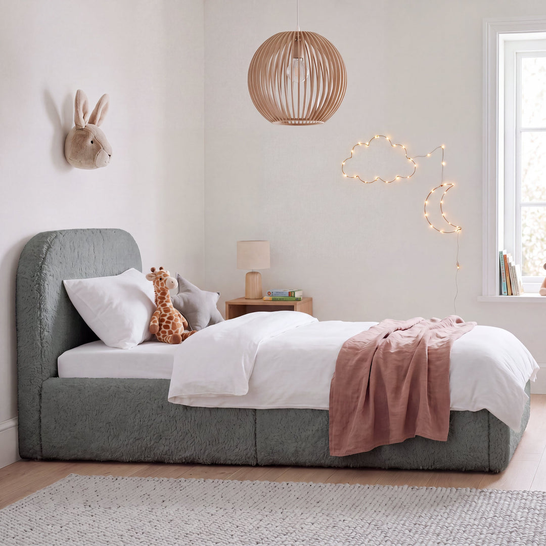 Grey bouclé children's bed with fall protection, cuddly toys and wooden lamp in a children's room. Fully AI-generated.