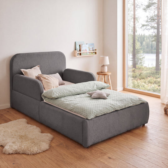 Letto grigio in bouclé con lampada da comodino, libreria e vista sul bosco nella stanza. Interamente generata con IA.