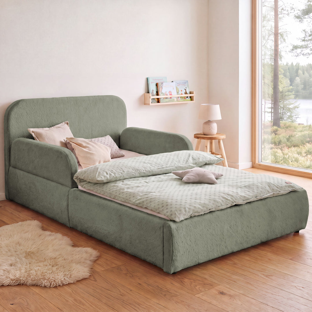 Letto per bambini roba Little Dream verde salvia in una cameretta con vista lago, libreria e tappeto in pelle di pecora. Parzialmente generata con IA.