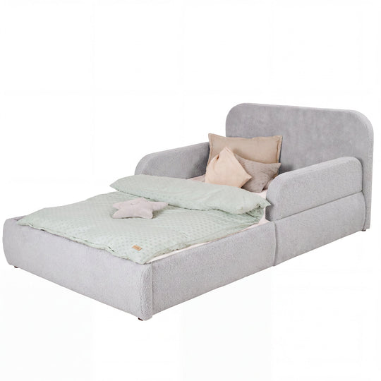 Cama infantil roba Little Dream gris claro con cabecero y protecciones laterales, vestida con ropa de cama y cojines. Generada parcialmente con IA.
