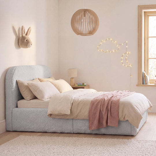 Cama infantil roba Little Dream gris claro en una acogedora habitación infantil con lámpara colgante y guirnalda de luces. Generada parcialmente con IA.