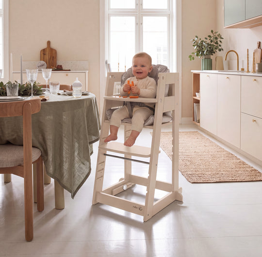 Vergleichsbild: links ein Baby im Cashmere-farbenen Lernturm in Hochstuhl-Konfiguration mit Sternkissen, rechts ein lachendes Kleinkind, das in der Steh-Konfiguration steht; am Lernturm hängt ein Anhänger mit der Aufschrift 'SIT & STEP'.