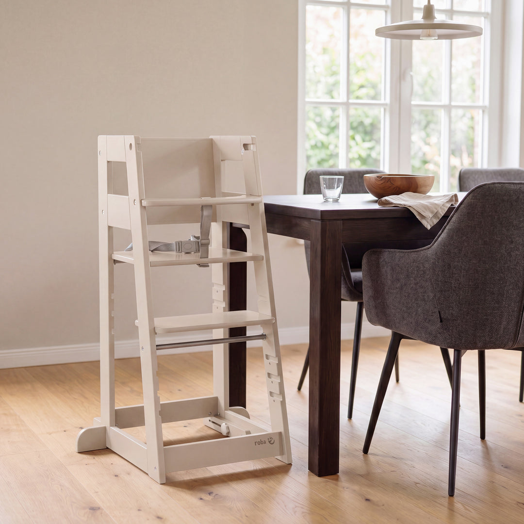 Lifestyle: Mutter und Kleinkind sitzen an einem gedeckten Esstisch mit Kerzen und Grünpflanzen, das Kind sitzt im Lernturm 'Sit & Step' in Cashmere in der Hochstuhl-Konfiguration.