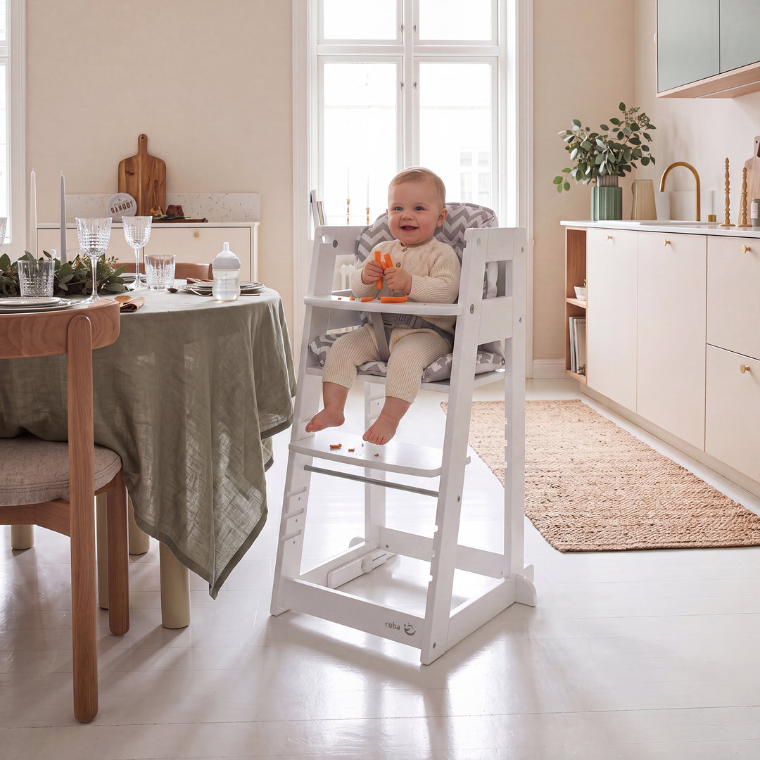 Vergleichsbild: links ein Baby im weißen Lernturm in Hochstuhl-Konfiguration mit Sternkissen, rechts ein lachendes Kleinkind, das in der Steh-Konfiguration steht; am Lernturm hängt ein Anhänger mit der Aufschrift 'SIT & STEP'.