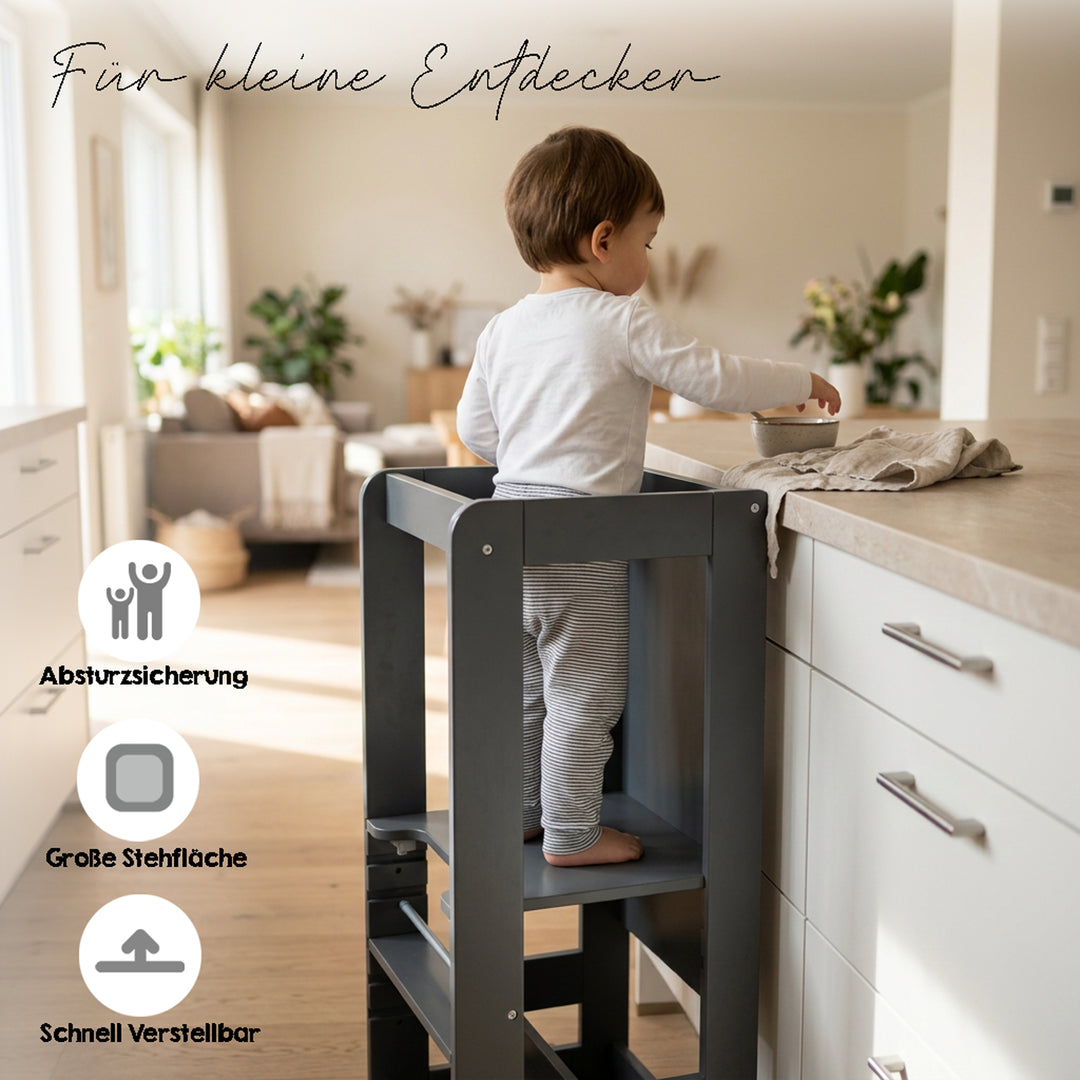 Lifestyle-Bild mit Schriftzug 'Für kleine Entdecker' und Symbolen für Absturzsicherung, große Stehfläche und schnelle Verstellbarkeit; Kleinkind steht im Anthrazit-Lernturm an einer Küchenarbeitsplatte.