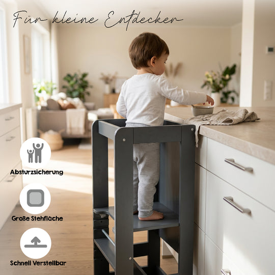 Lifestyle-Bild mit Schriftzug 'Für kleine Entdecker' und Symbolen für Absturzsicherung, große Stehfläche und schnelle Verstellbarkeit; Kleinkind steht im Anthrazit-Lernturm an einer Küchenarbeitsplatte.